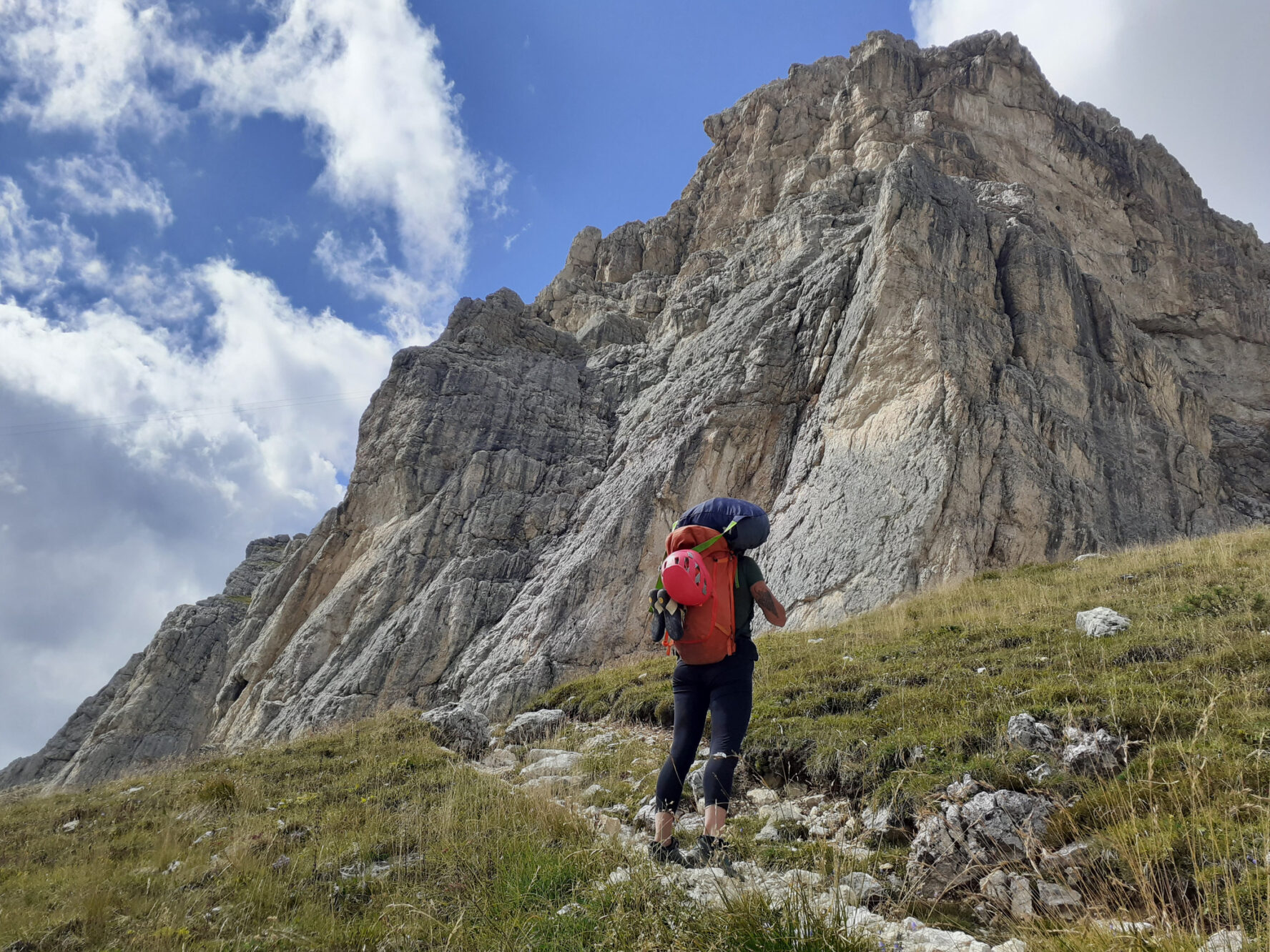A rock climber standing next to a massive rock formation in the Dolomites.