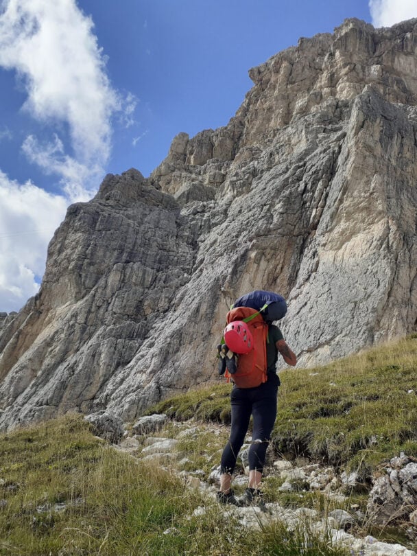 A rock climber standing at the foot of a Dolomite wall at the high elevation with views of Cortina d’Ampezzo and its valley and surrounding mountains.