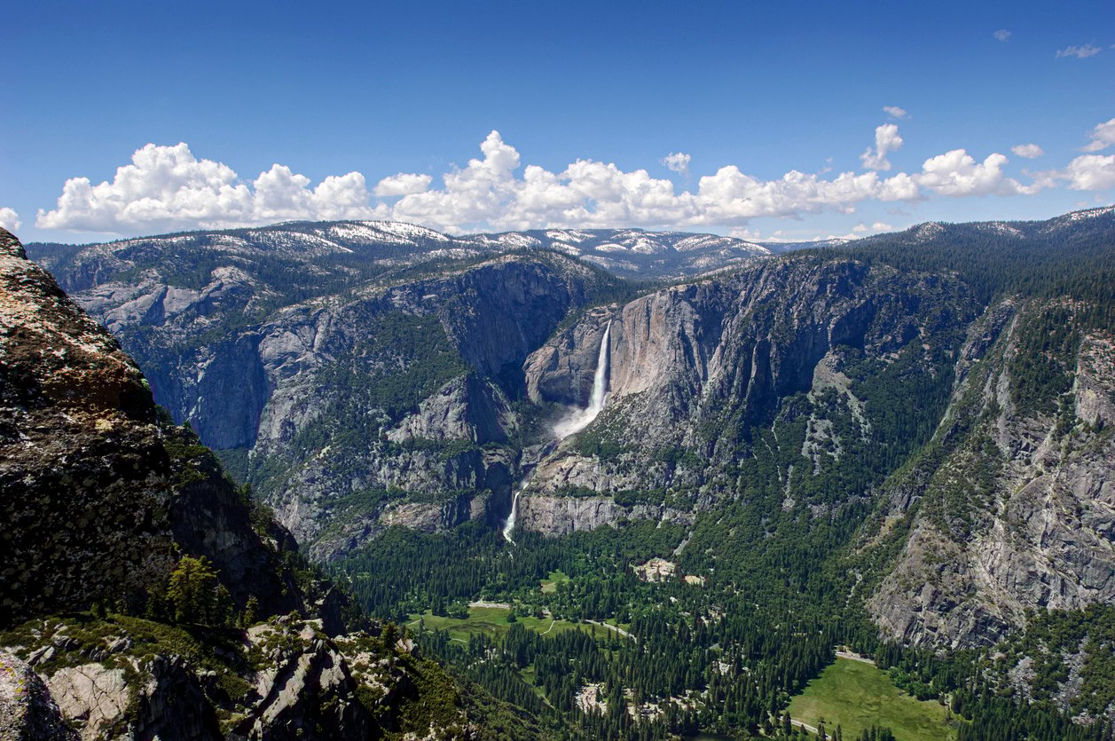 Sprawling view of Yosemite landscapes with dramatic granite walls, a waterfall and a forest as seen from the Glacier Point.