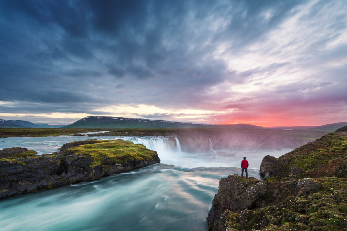 Hiker standing on a cliff watching the Godafoss waterfall in Iceland 