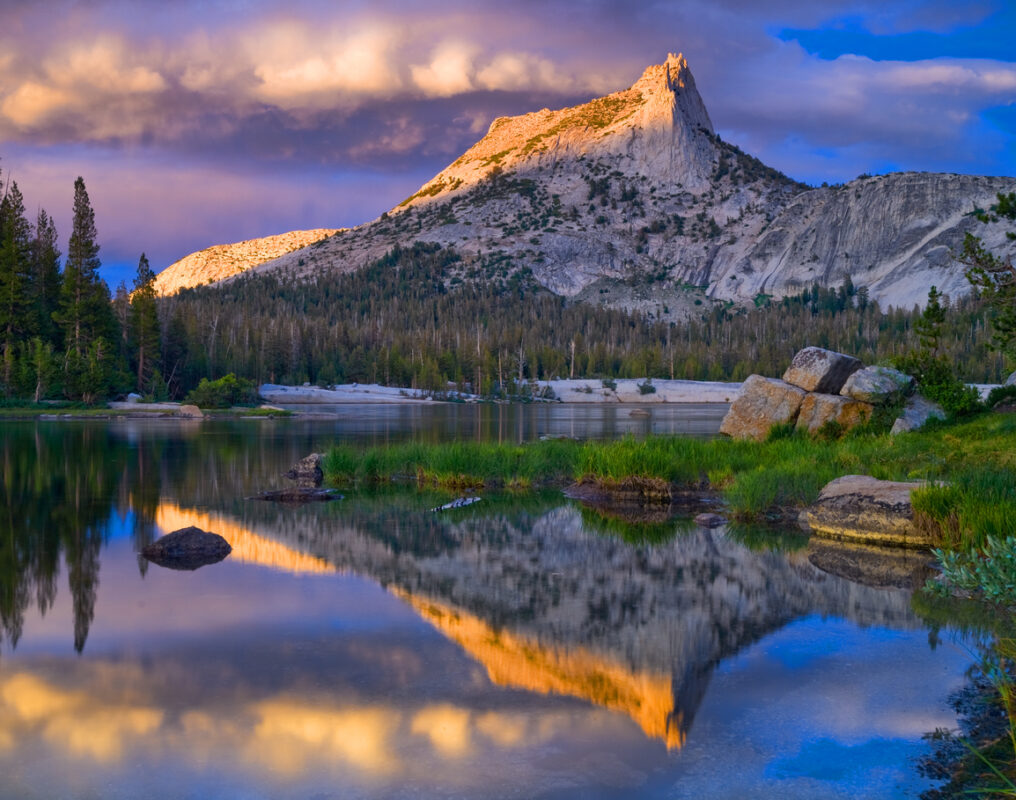 Yosemite’s Upper Cathedral Lake during sunset, surrounded by conifers and with a lofty granite peak in the distance. 