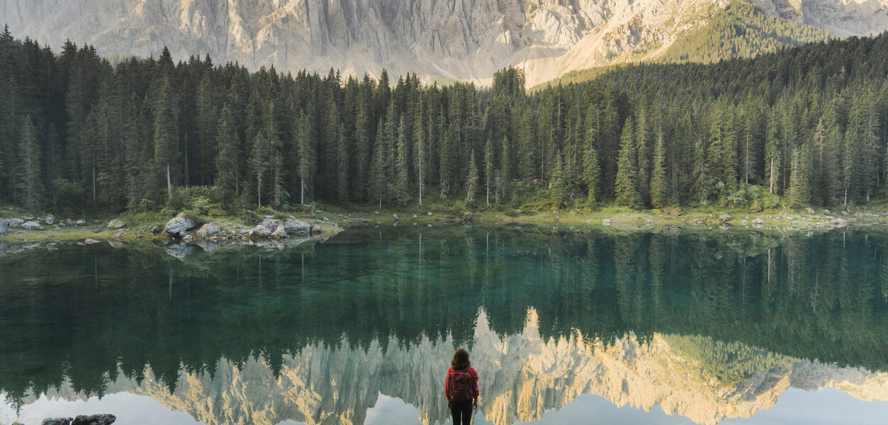 Woman standing in front of Lago di Carezza in the Dolomites, a perfect place for an all-women trip.