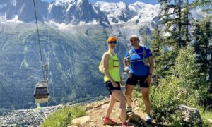 Two people posing on a hiking trail in the mountains of Chamonix with a gondola running behind them.