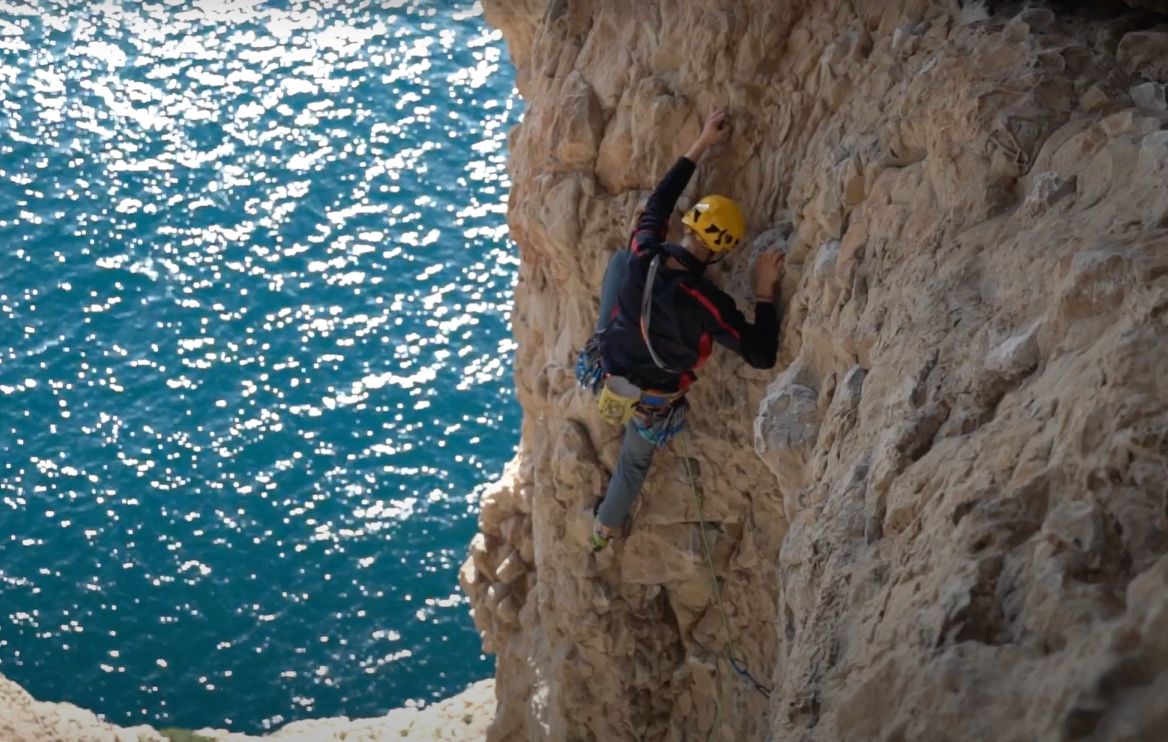 Glistening sea on the Costa Blanca below a climber climbing a route directly above.