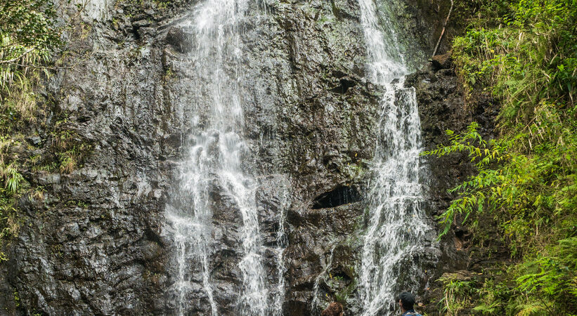 Pair of hikers standing under a small waterfall on the Ka’au Crater Trail