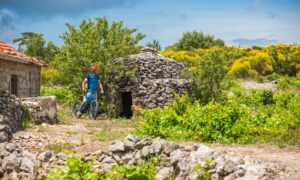 An MTB rider blazing by a stone house in Bunja, Hvar.