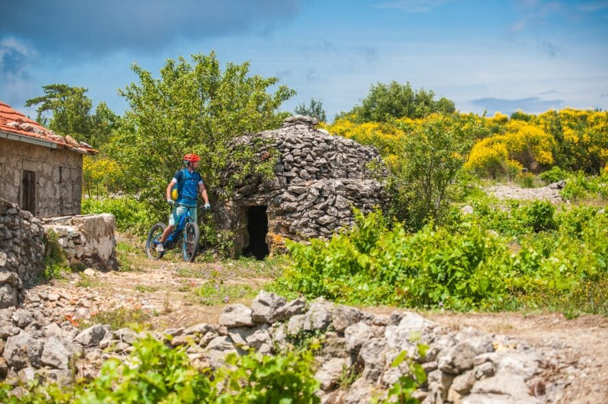 An MTB rider blazing by a stone house in Bunja, Hvar.