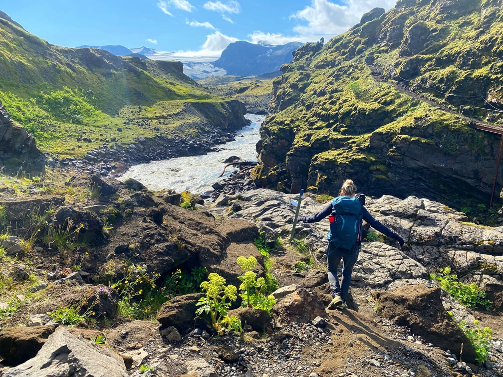A hiker descending the Laugavegur Trail in Iceland with a river and mountains in the background.