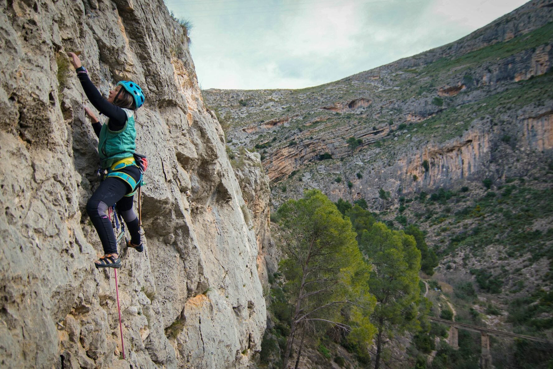A climber in the middle of a route across a vertical wall in the Alicante mountains.