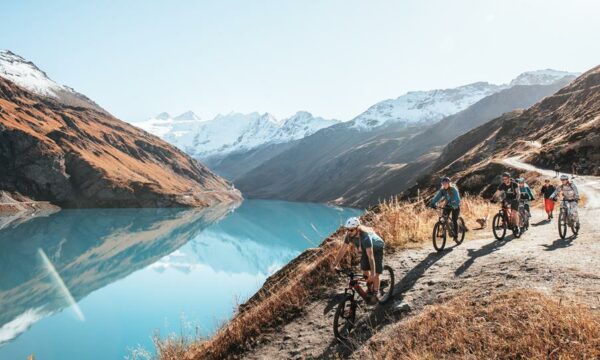 E-mountain bikers riding beside an Alpine lake during their Haute Route traverse.