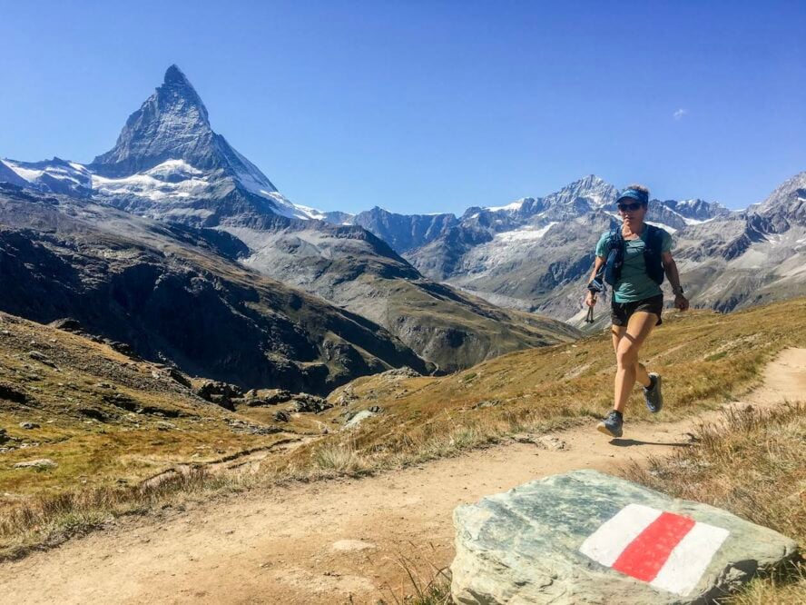 A woman running on the trail in Zermatt with the Matterhorn right behind her.