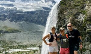 Three runners stopped for a photo in front of a waterfall with Zermatt in the background.