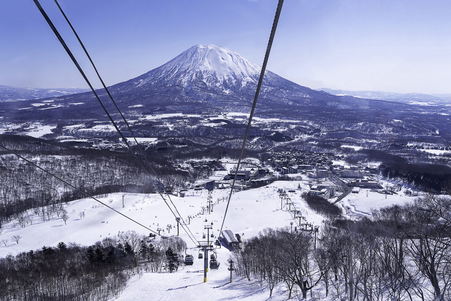 A ski resort with a gondola and a volcano shape mountain in the background.
