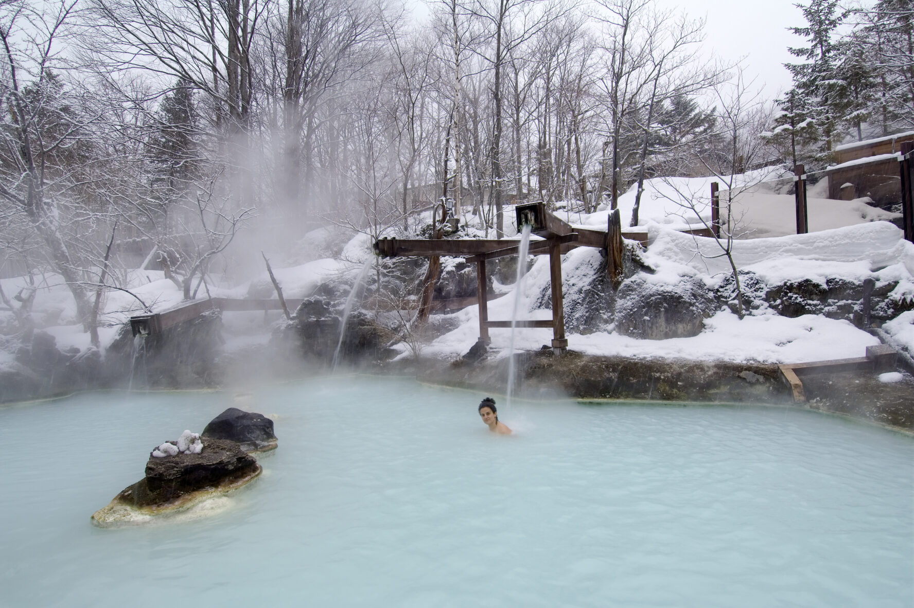 A person in a natural hot spring while the outskirts are covered in snow.
