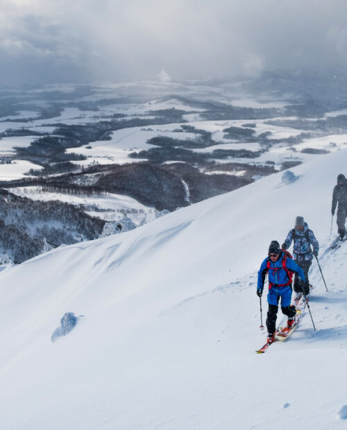 Three people going uphill on a ski tour with fog and snow in the background.