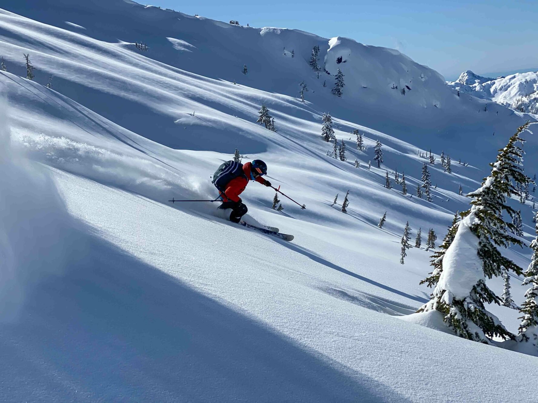 Person with a red jacket skiing down the face of a mountain on untouched snow.