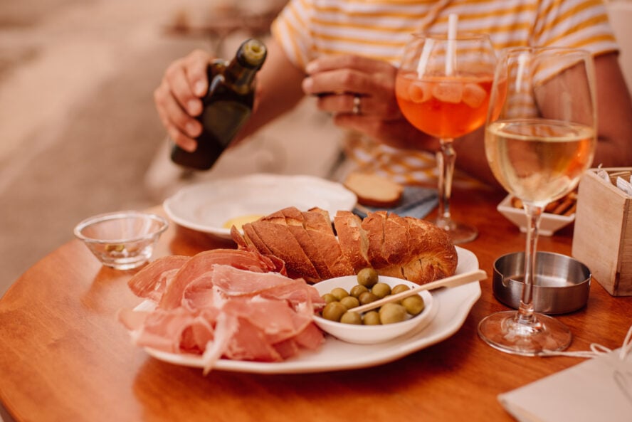 A plate with olives, cured ham and bread, with some olive oil.