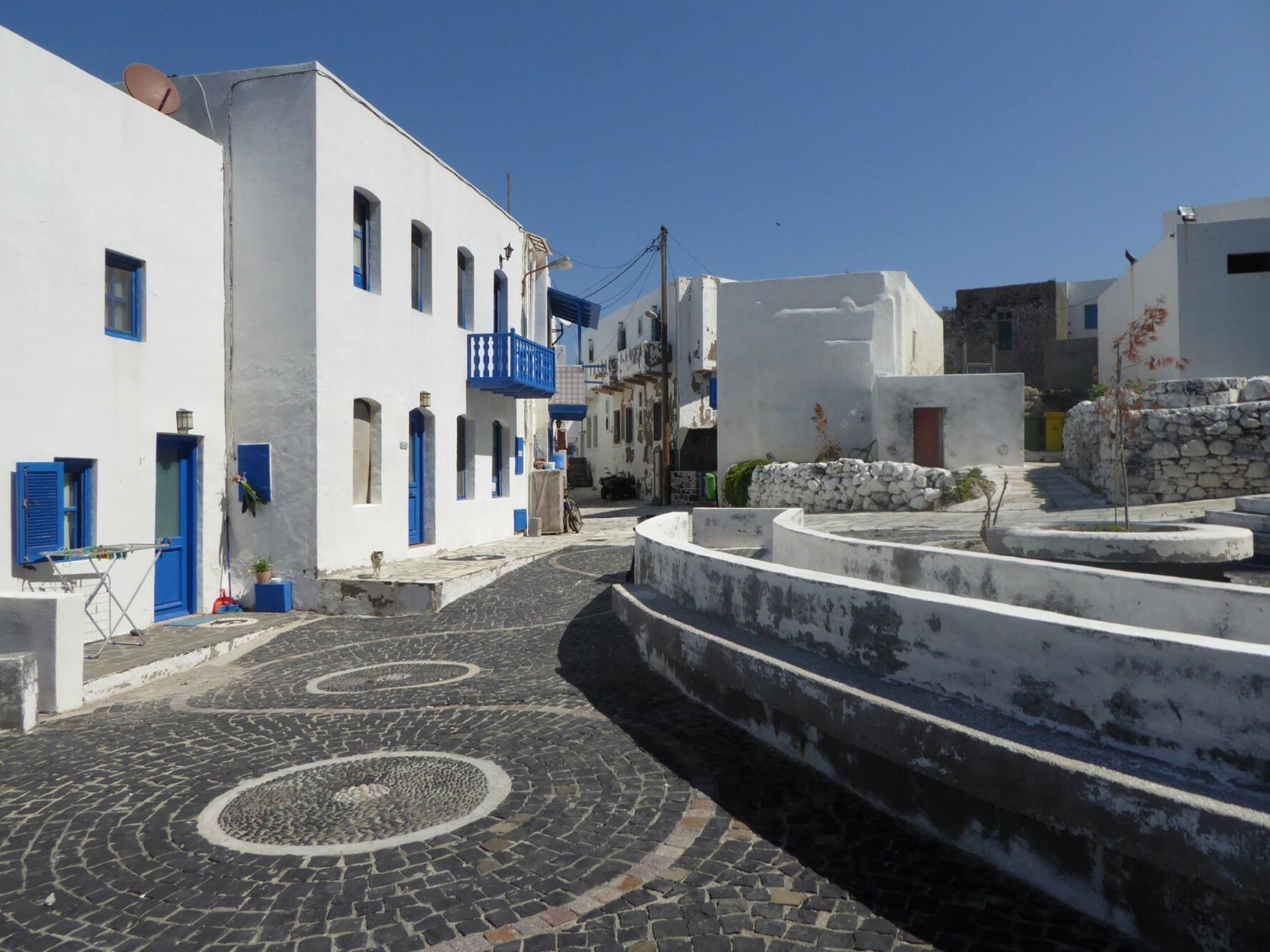 A square enclosed by white houses with blue shutters in the village of Mandraki on the Greek island of Nisyros.
