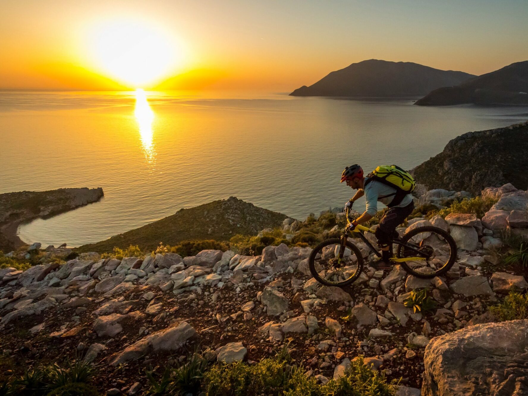 A mountain biker riding by the scenic coast on the Greek island of Tilos during sunset.