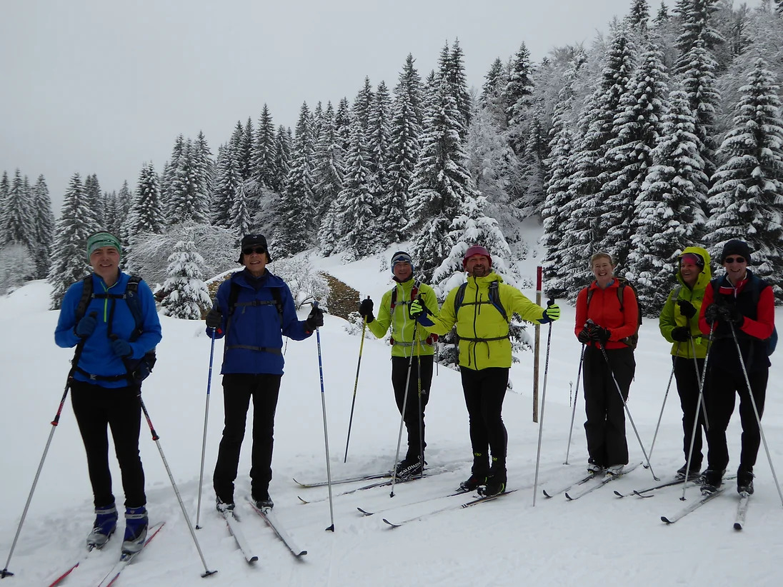 Cross-country skiers posing for a picture while on a trail in Italy surrounded by snow-covered conifer trees.