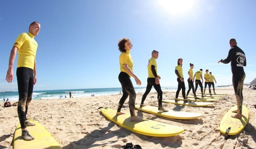 Participants of a surf school in Fuerteventura standing beside the shore and listening to their Fuerteventura surf teacher.