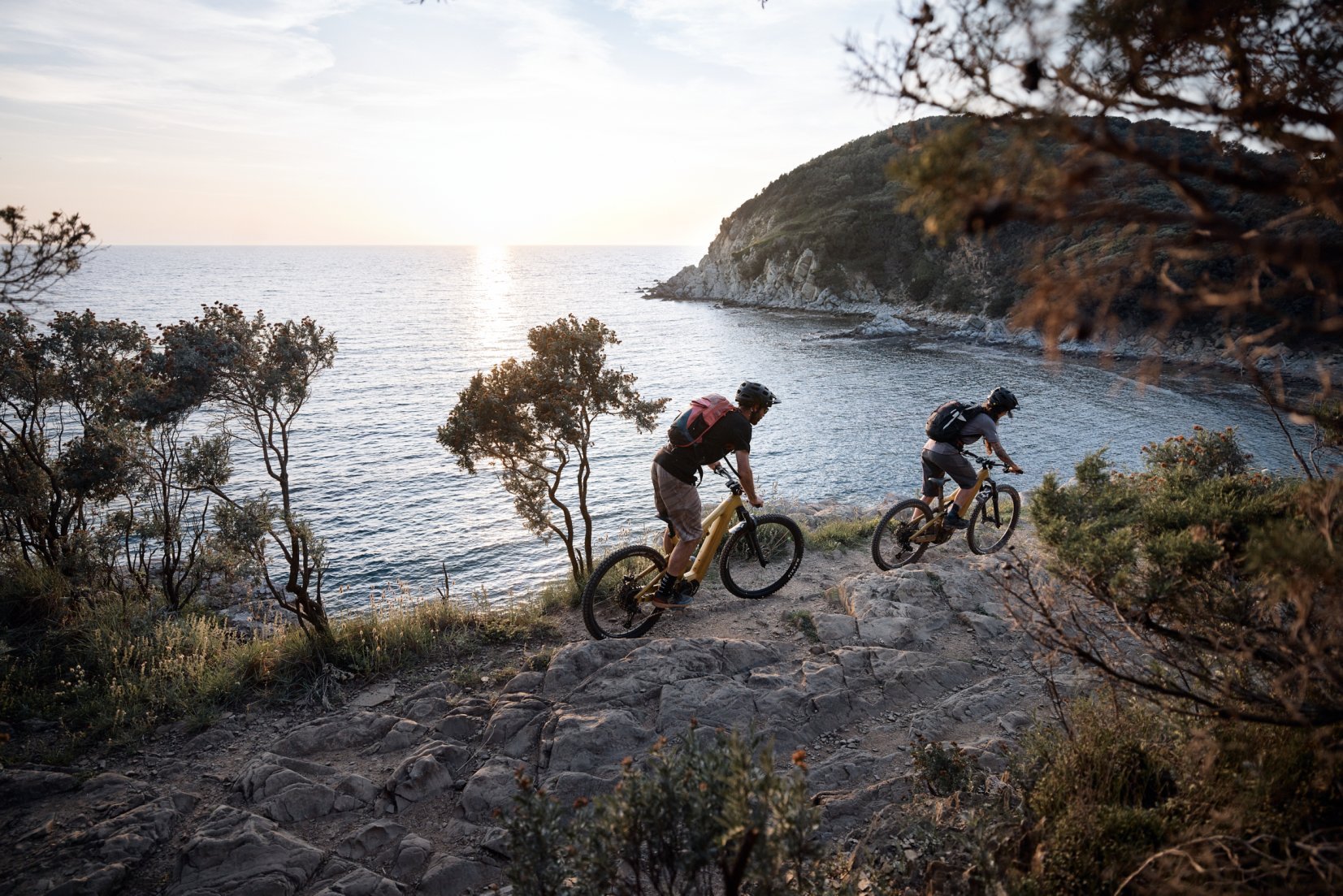 E-mountain bikers riding a trail beside the rugged coast near Piombino, Tuscany.