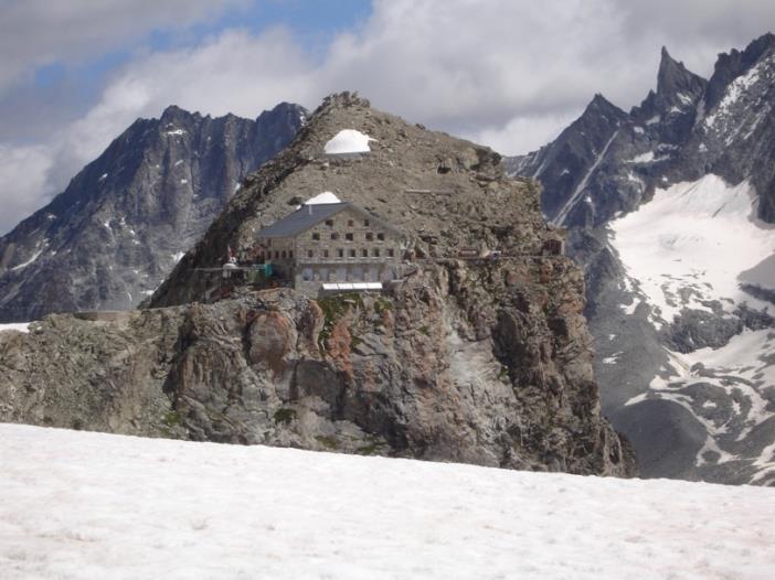 A mountain hut in a rugged location, surrounded by bare mountains and icy sections, in the Swiss Alps, along the Haute Route Glacier Trek.