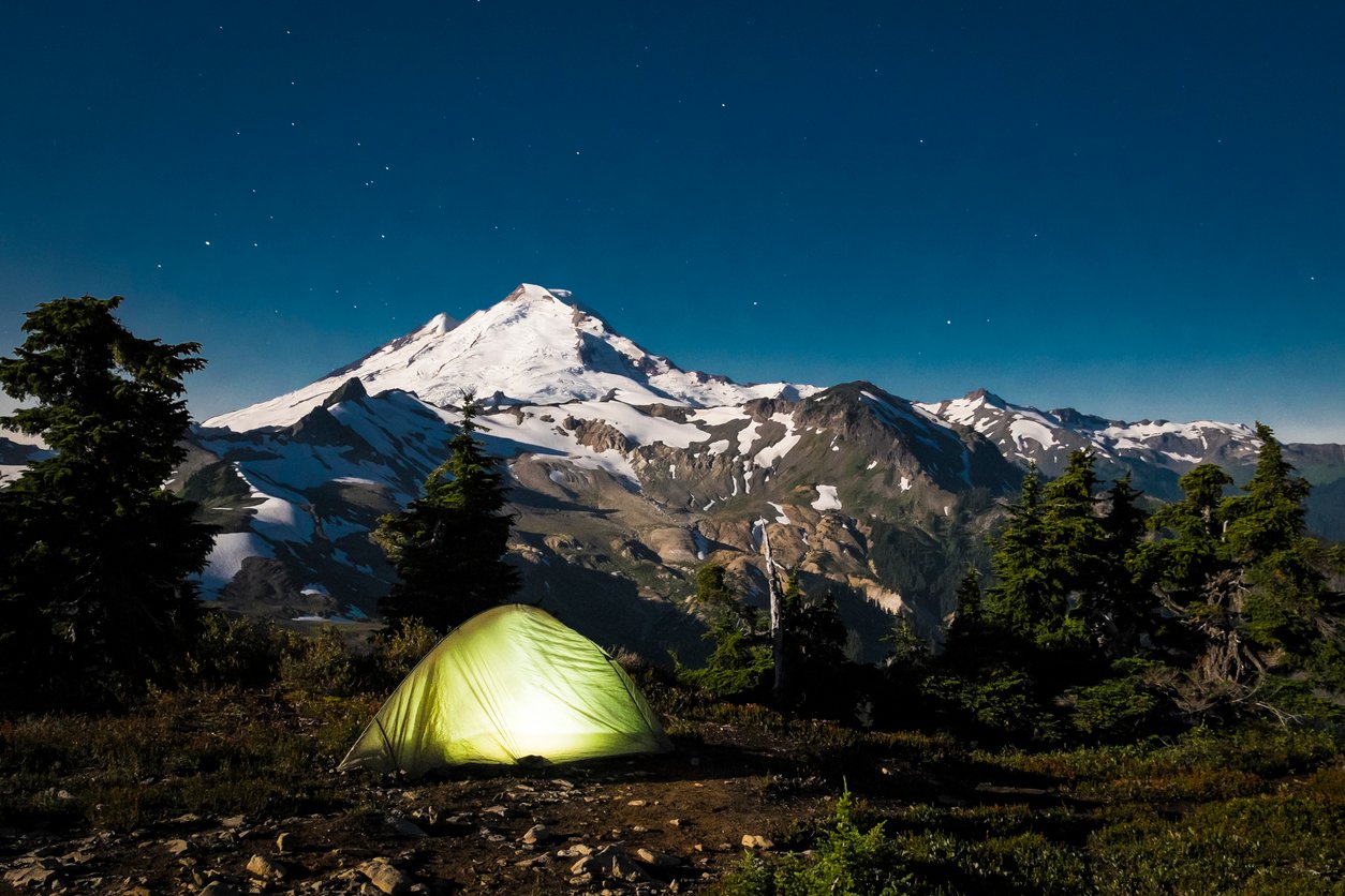 A campsite at the foot of Mt Baker seen at dusk, with a glowing tent.