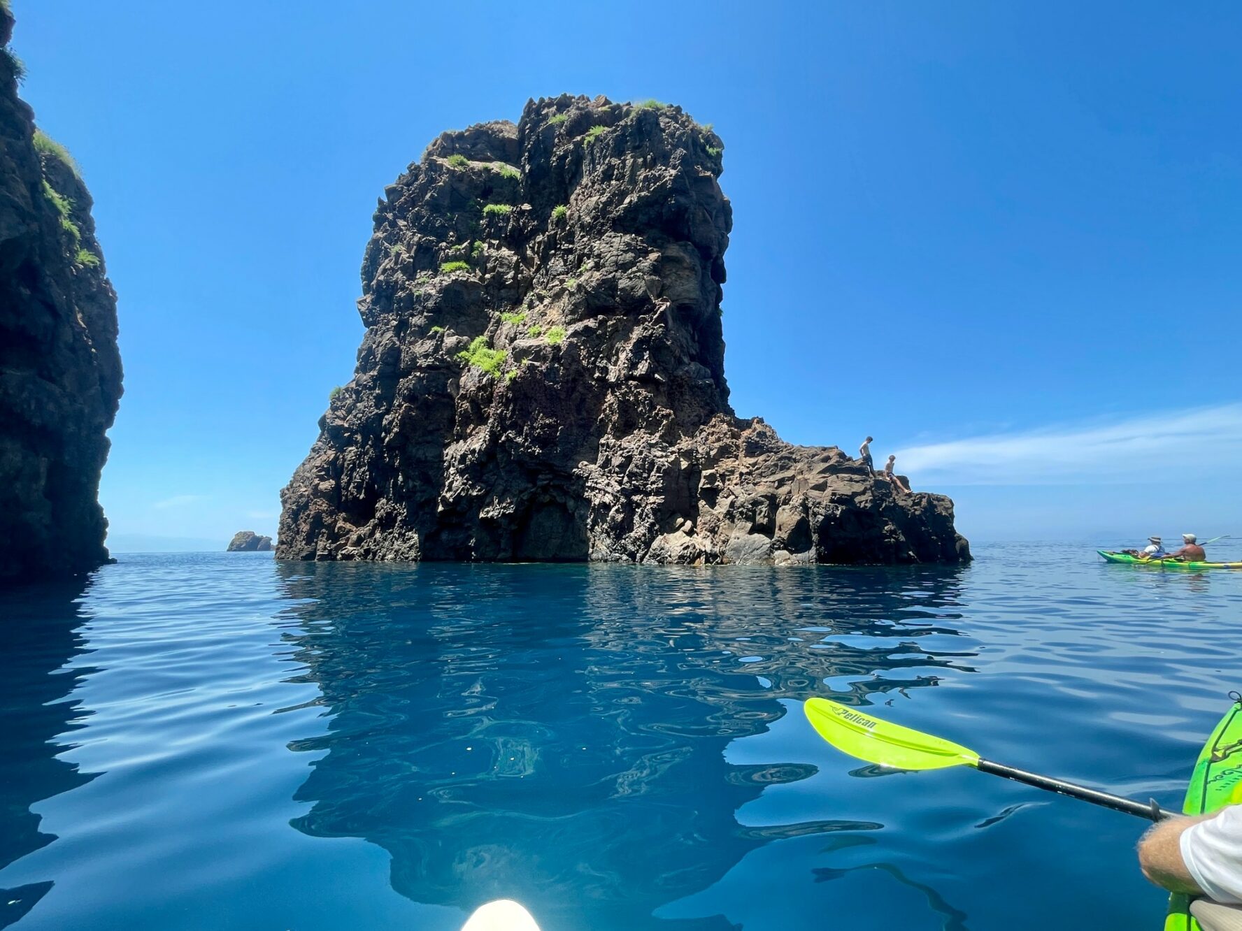 Kayakers paddling around a rugged islet in the Aeolian Islands, Italy.