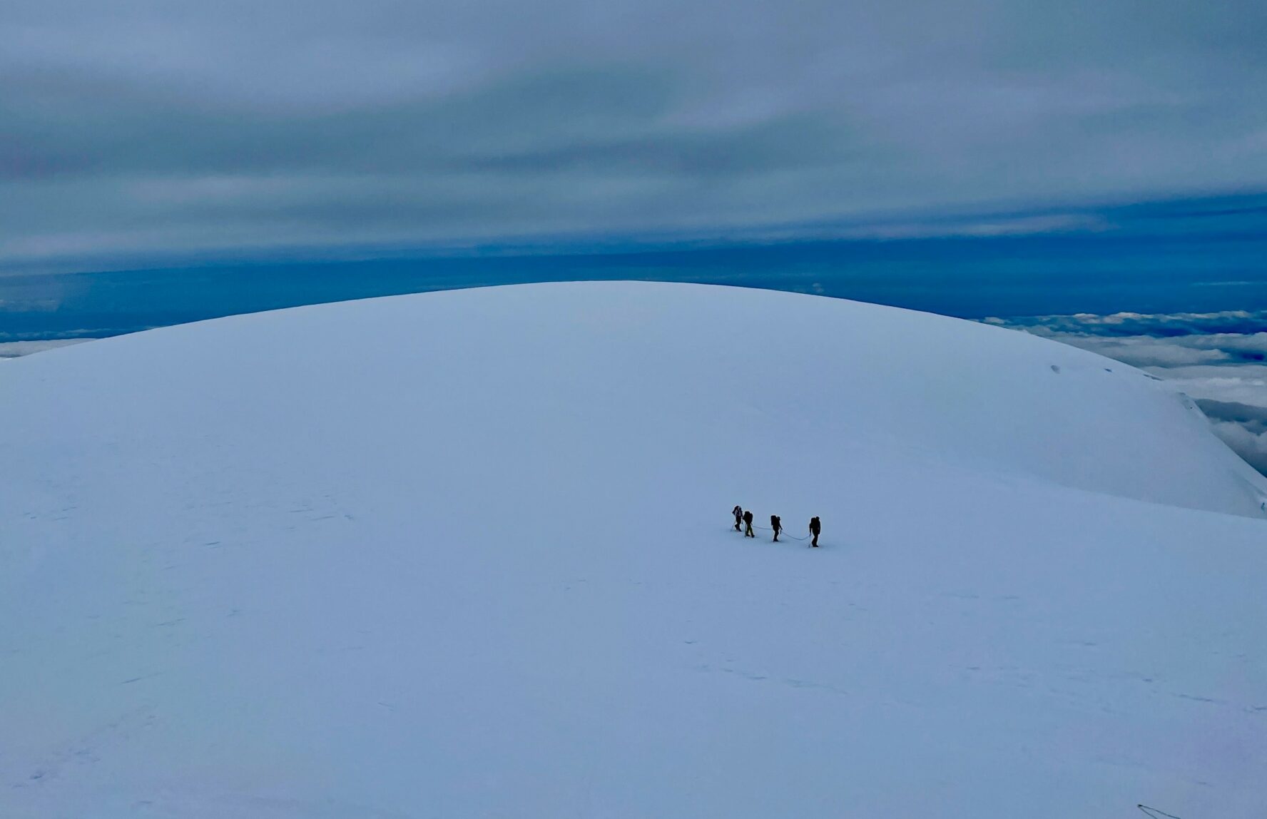 Three mountaineers seen from the distance on Mount Baker navigating a large, snowy expanse.
