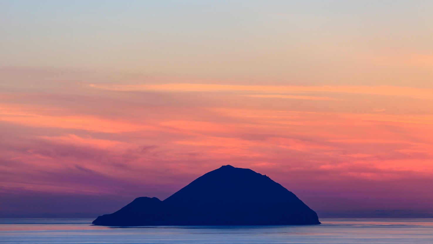A volcanic island in Italy seen from a distance during sunset.
