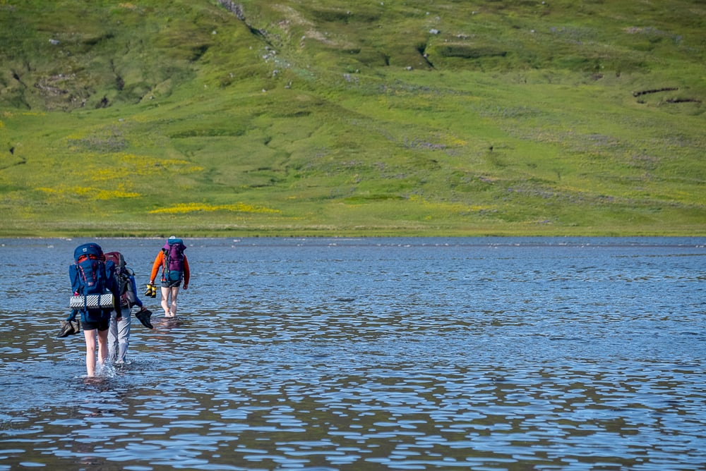 Backpackers crossing a river in the Hornstrandir Nature Reserve, Iceland.