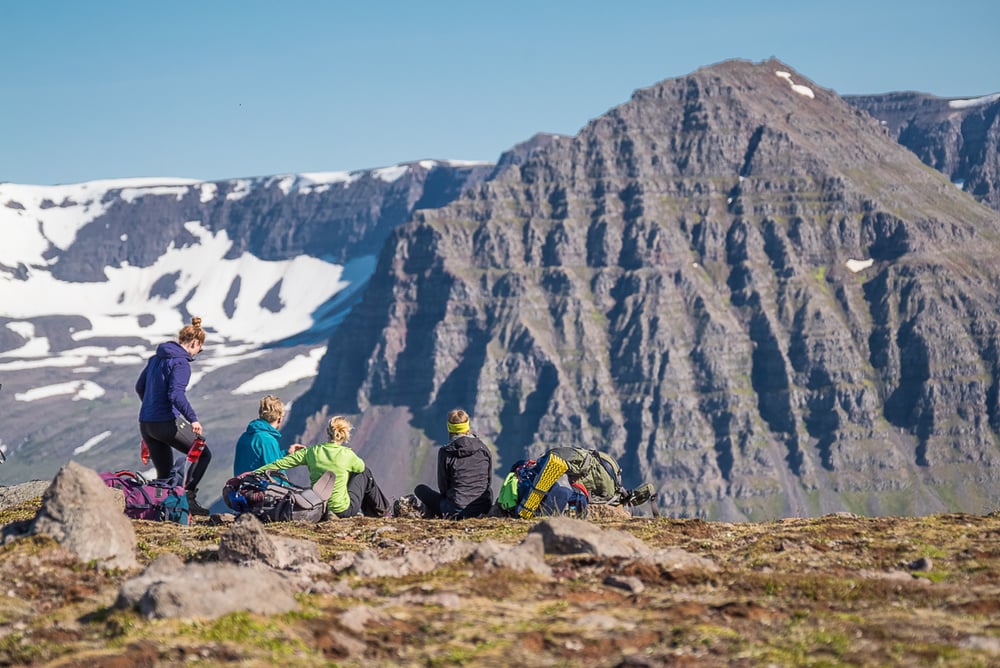 Trekkers enjoying the view of steep basalt mountains with snow patches in Hosnstrandir, Westfjords, Iceland.
