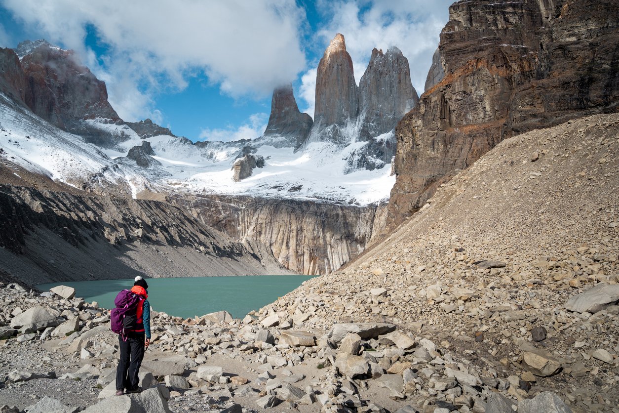 A woman hiker near a turquoise lake near granite spires, along the W Circuit.