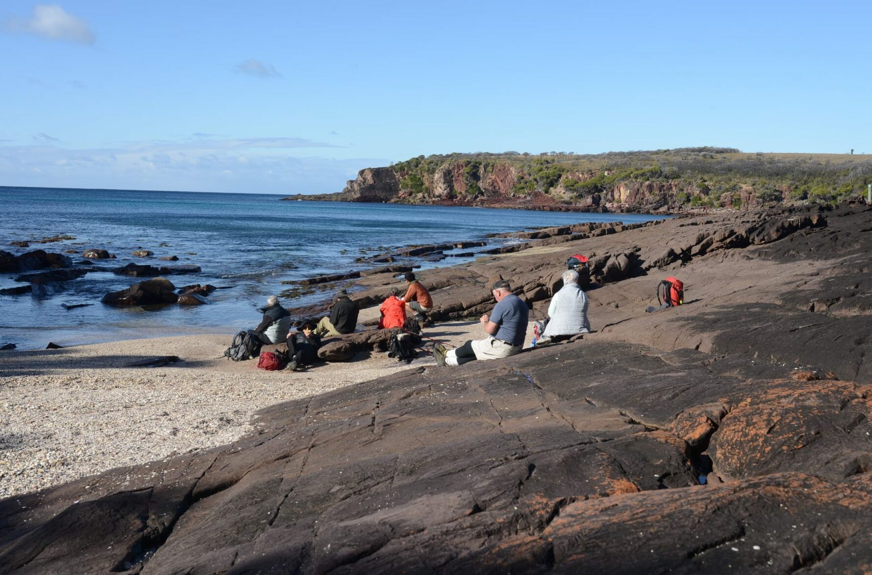 Hikers resting on a rugged beach during their Light to Light hiking adventure in NSW, Australia.