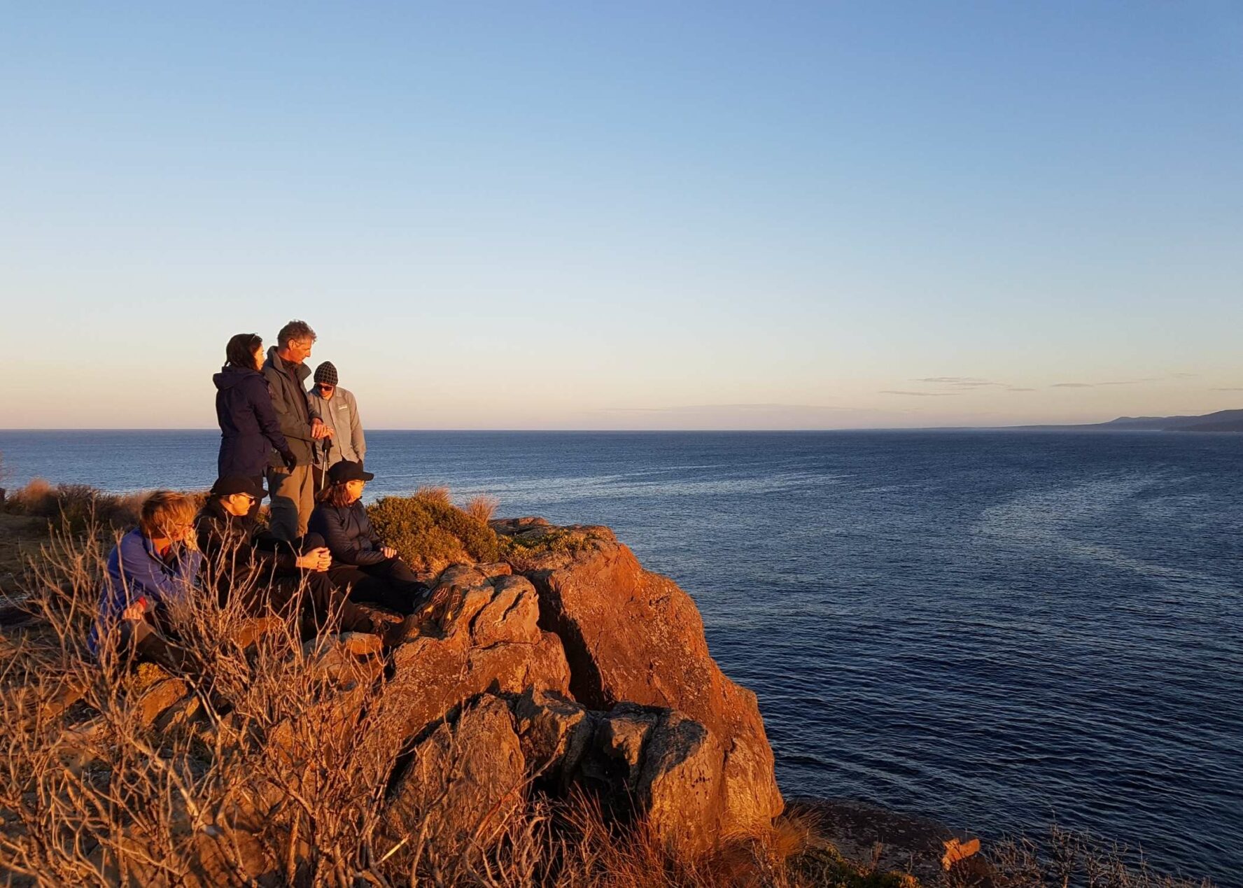 Hikers at sunset atop a cliff along the Light to Light Walk in Australia.
