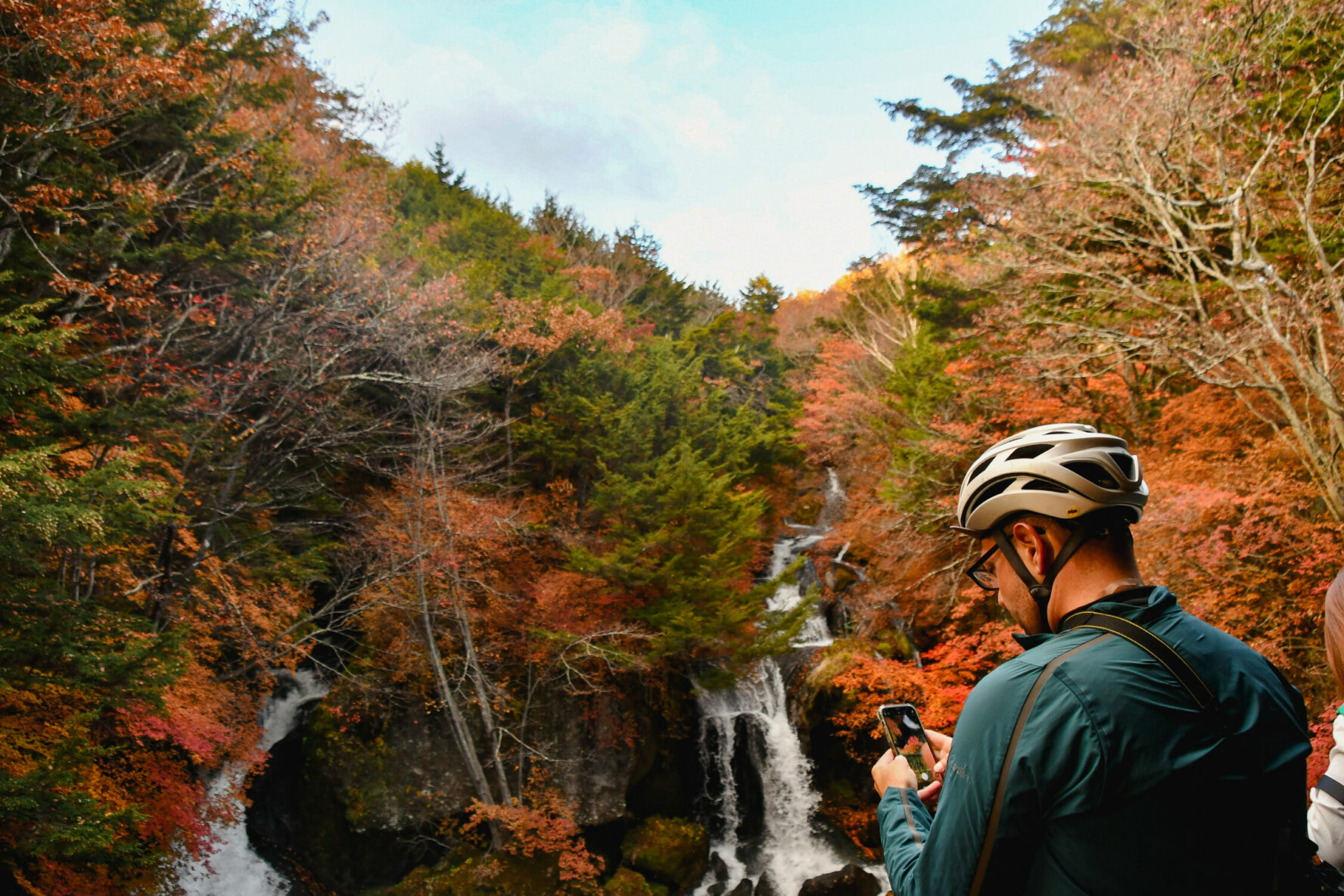 A cyclist looking at a waterfall surrounded by trees in fall colors, in Japan, between Nasu and Nikko.