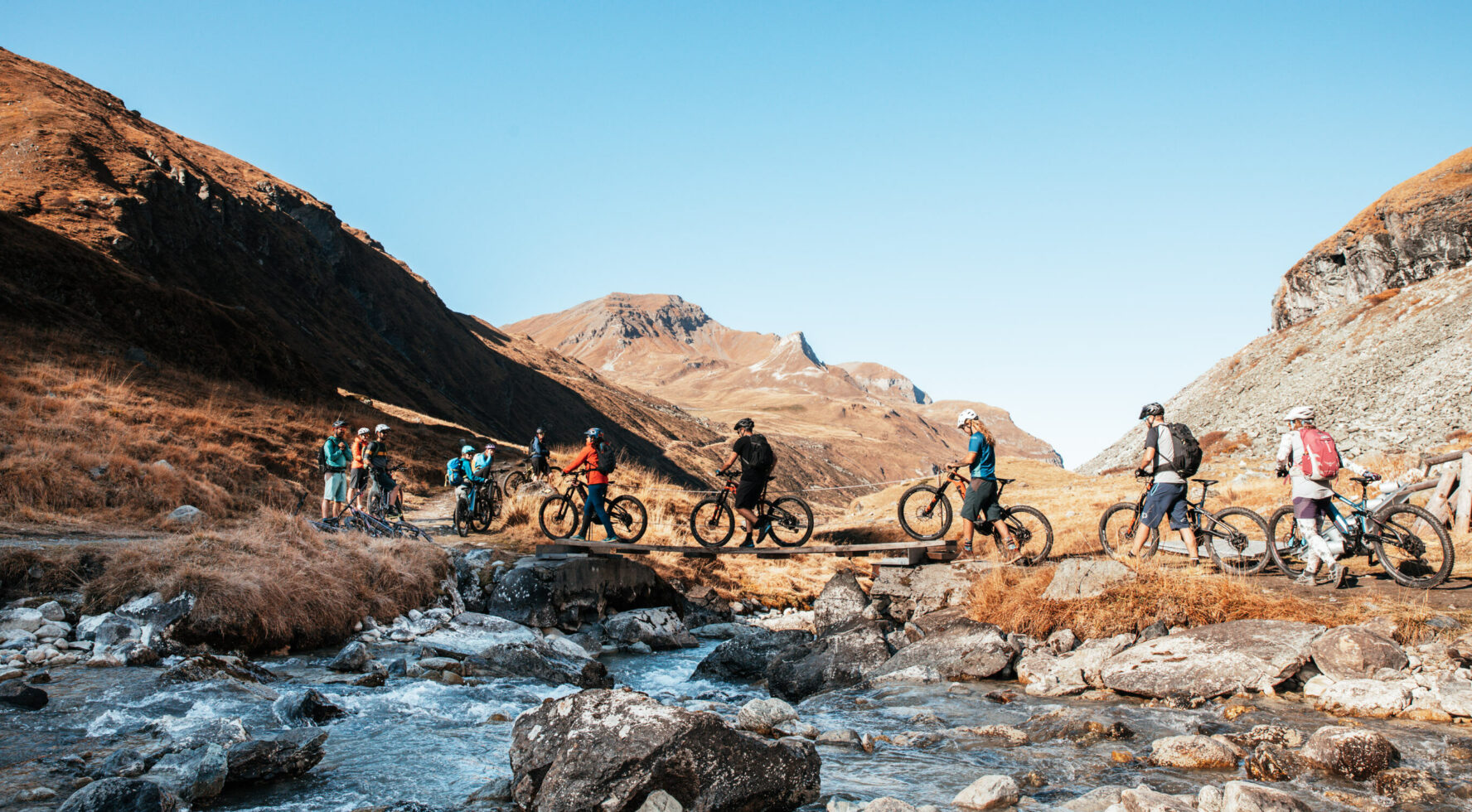 E-mountain bikers located next to a stream in the Swiss Alps, along the Haute Route.