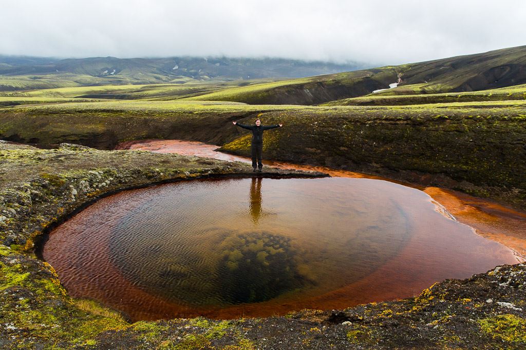 Hiker near a red river source in Iceland.