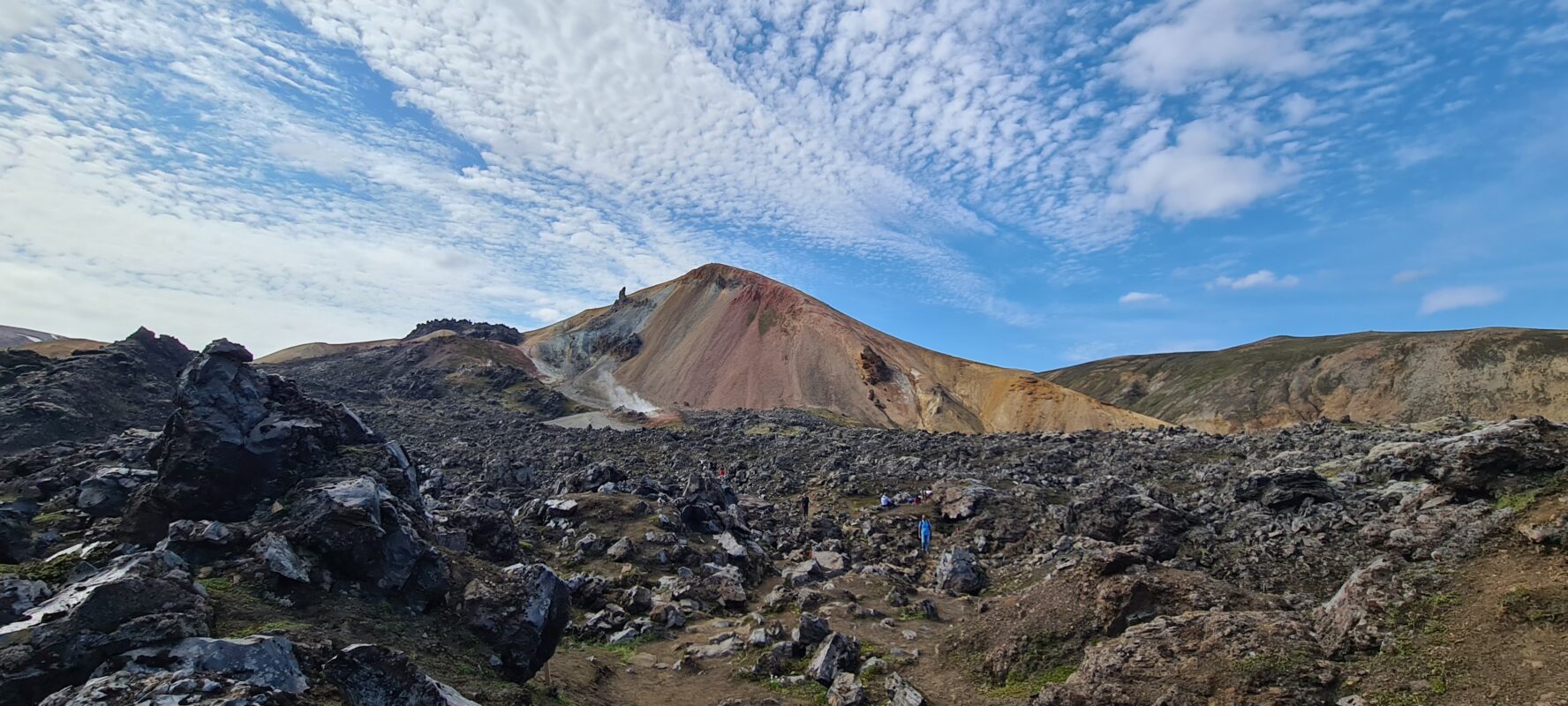 A hiker standing at the foot of a rhyolite mountain, in Iceland.