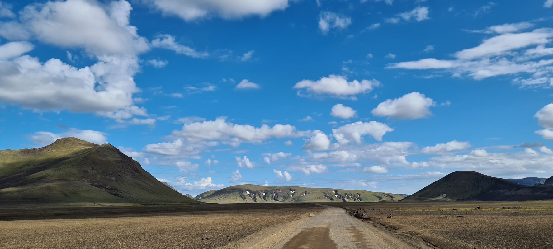 A road cutting through the Icelandic Highlands, surrounded by mountains.