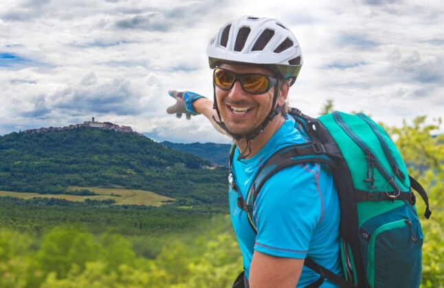A cyclist pointing at the medieval hilltop town of Motovun while located in the verdant Mirna Valley in Istria, Croatia.