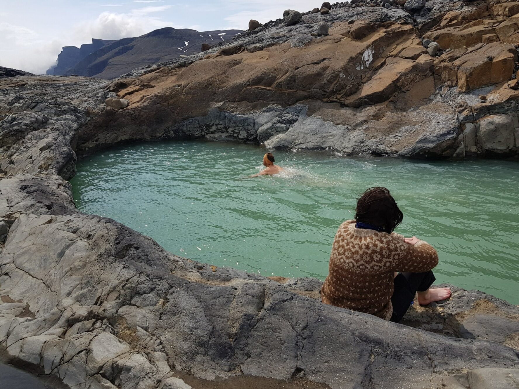 Hiker swimming in a small geothermal lake, Iceland.
