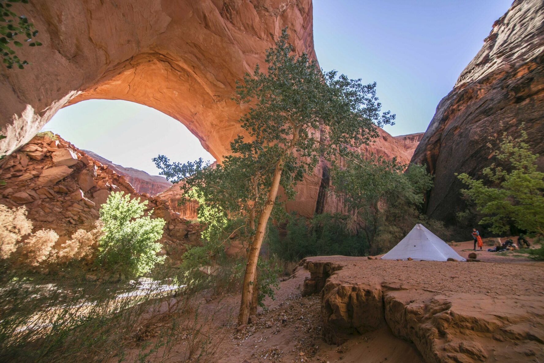 A tent in the Coyote Gulch, below a huge sandstone arch.