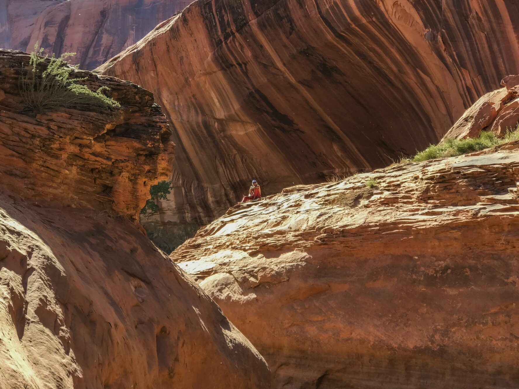 Backpacker admiring scenery while sitting atop a sandstone rock formation in Coyote Gulch.