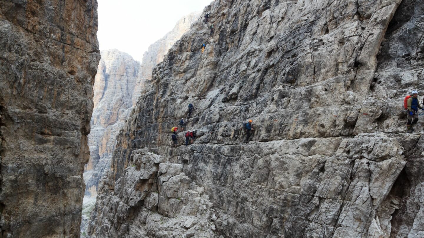 Via ferrata enthusiasts navigate a difficult section of Via delle Bocchette in the Dolomites, with a very narrow ledge.