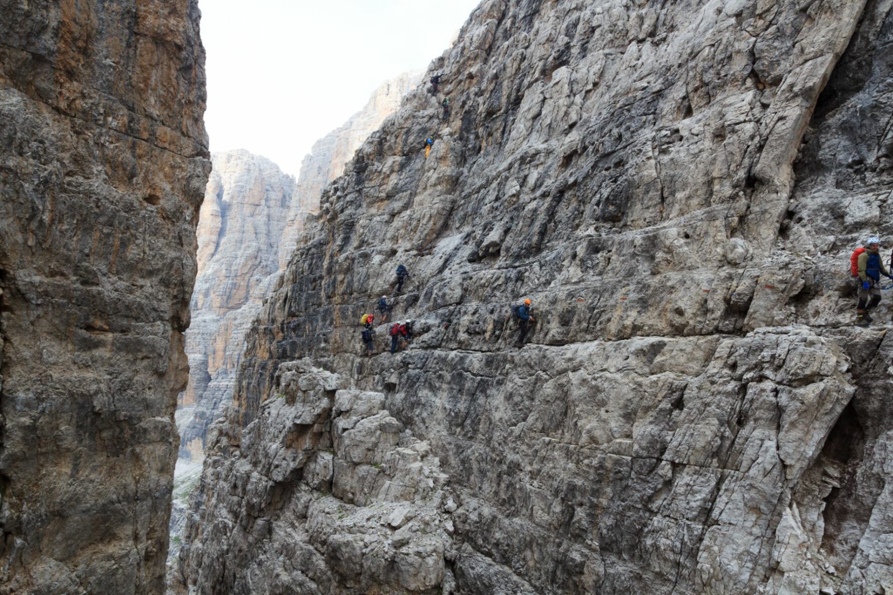 Via ferrata enthusiasts navigate a difficult section of Via delle Bocchette in the Dolomites, with a very narrow ledge.