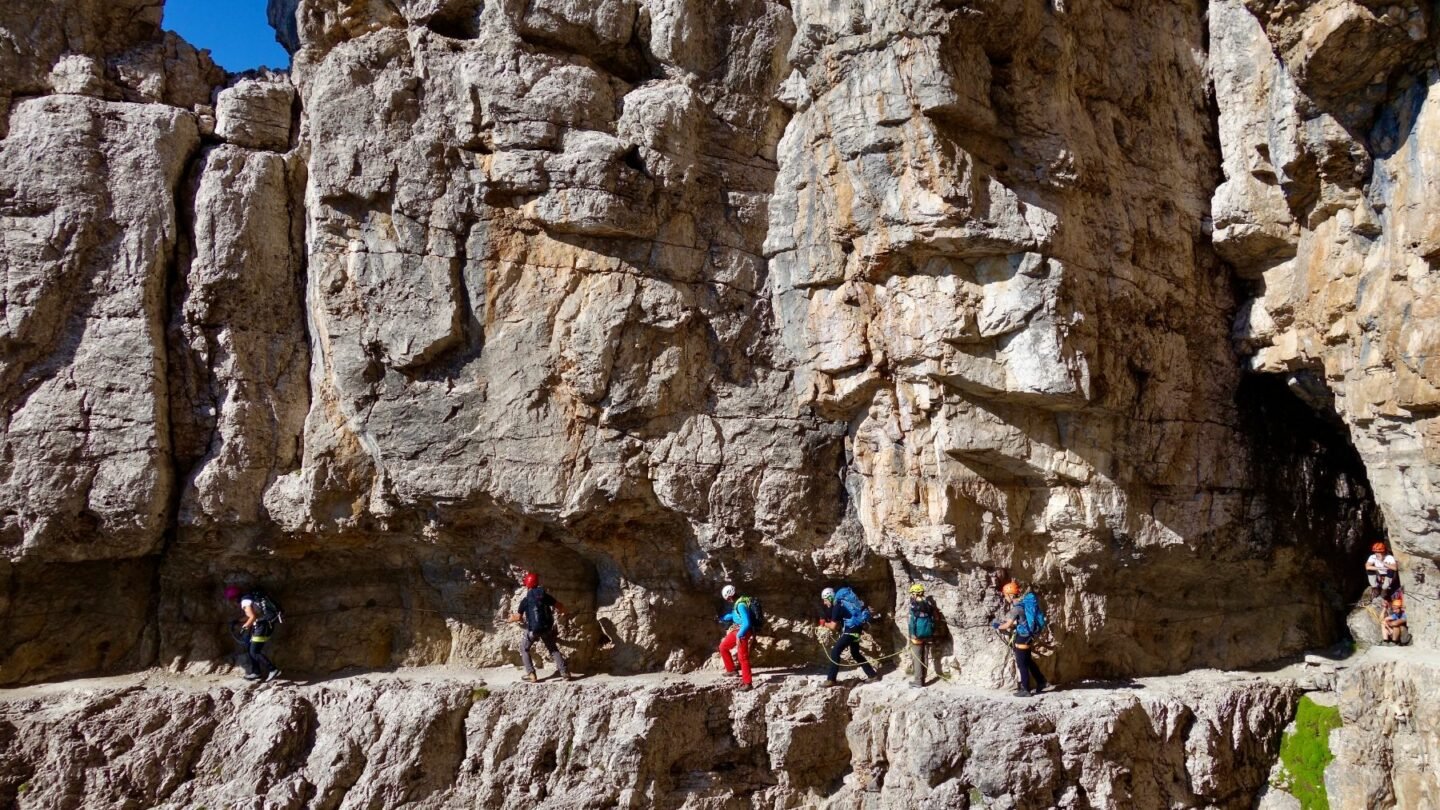 Via ferrata enthusiasts navigating a via ferrata right beside the reddish Dolomite rocks.