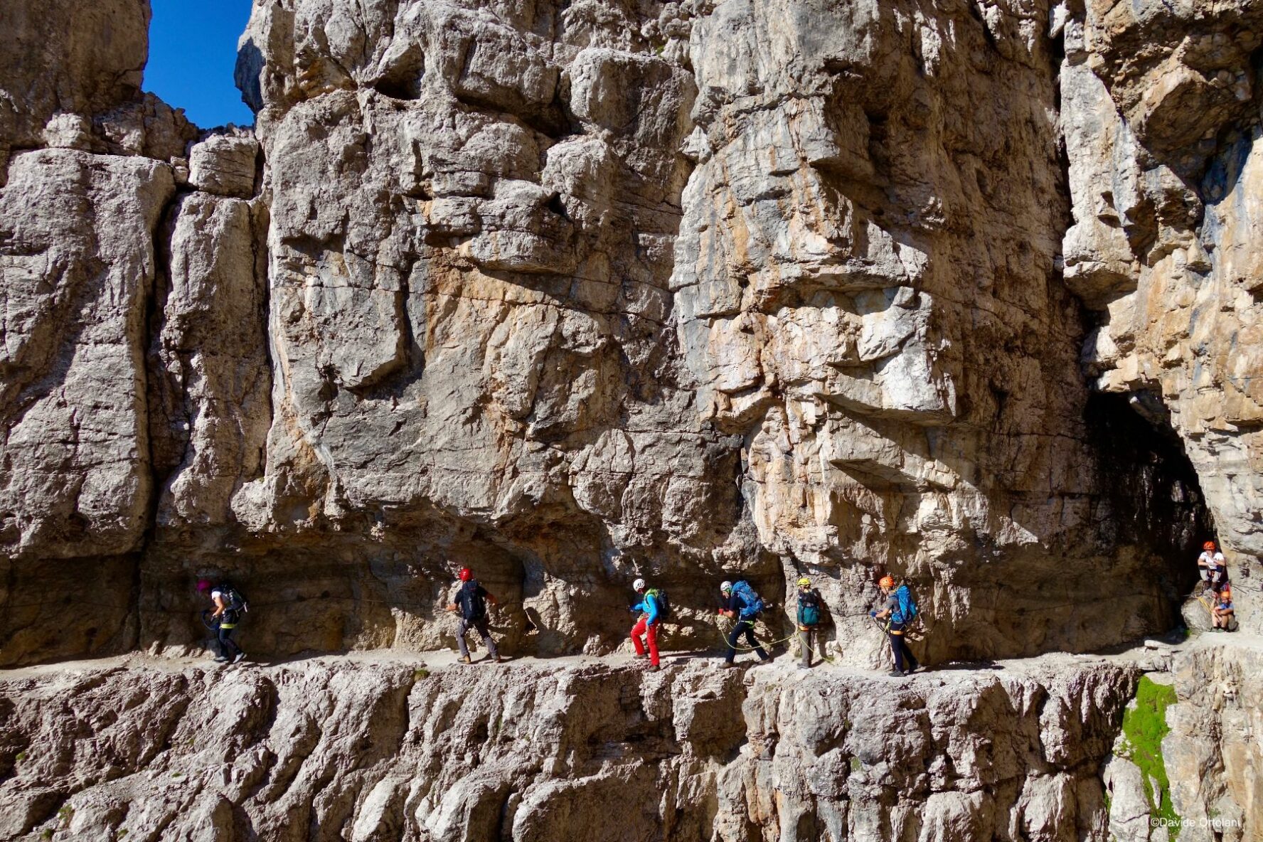 Via ferrata enthusiasts navigating a via ferrata right beside the reddish Dolomite rocks.