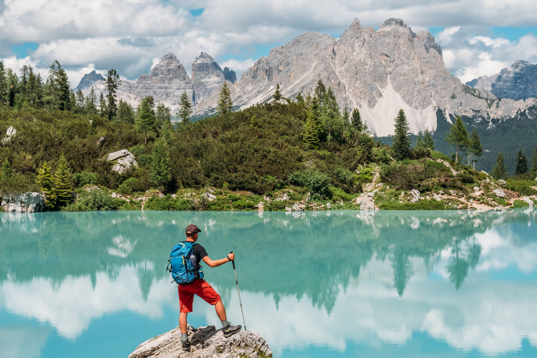 Backpacker with backpack enjoying the turquoise Lago di Sorapiss 1,925m altitude (mountain lake) view as he has mountain walk in Dolomite Mountains, Italy. Active people in nature concept.